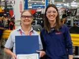 Two team members posing in front of the camera and one team member is holding a certificate of achievement